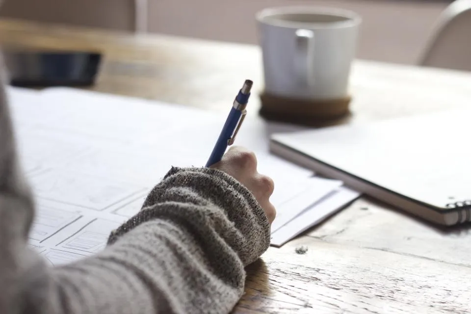 Iemand schrijft met pen aantekeningen op papier, naast een kop koffie.